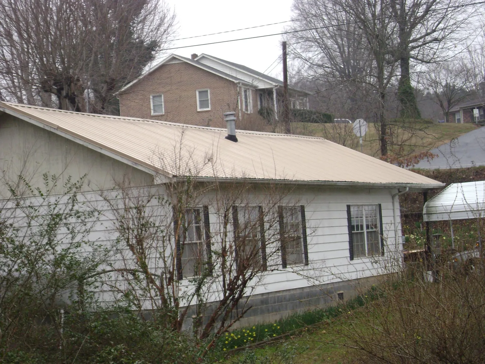 Tan metal roof on a white sided house set into a hillside — Commercial Roofing by Roofing Brothers in Thornton